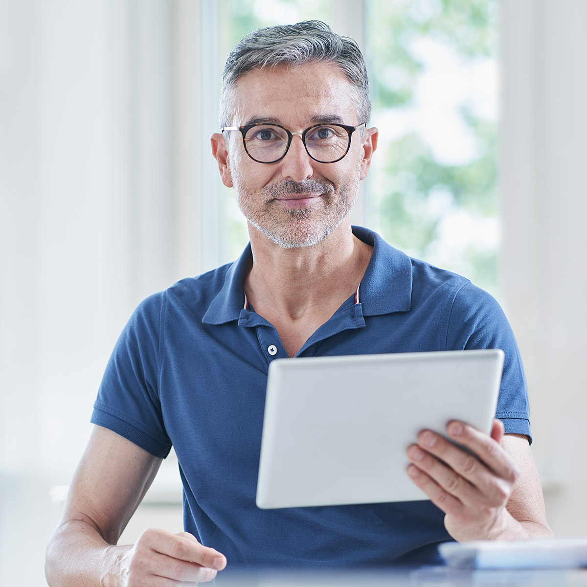 Mann lächelt in die Kamera und hält ein Tablet in der Hand