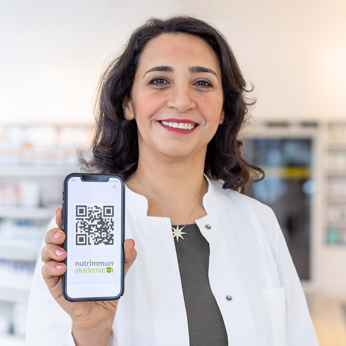 Apothekerin lächelt und hält Smartphone mit QR Code in dei Kamera