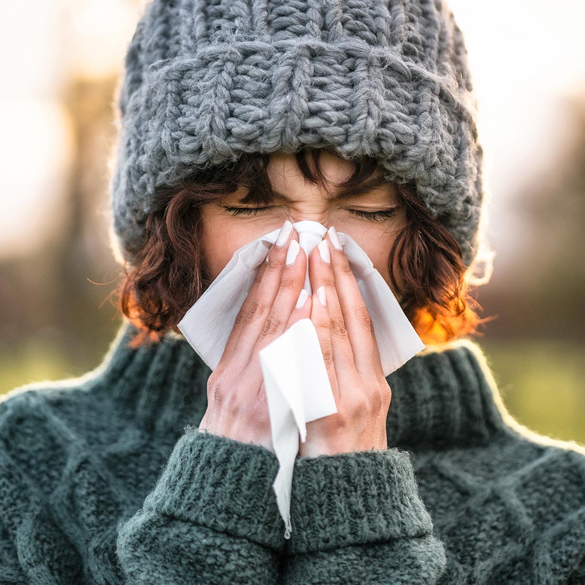 Frau mit grauer Mütze schnieft in ein Taschentuch