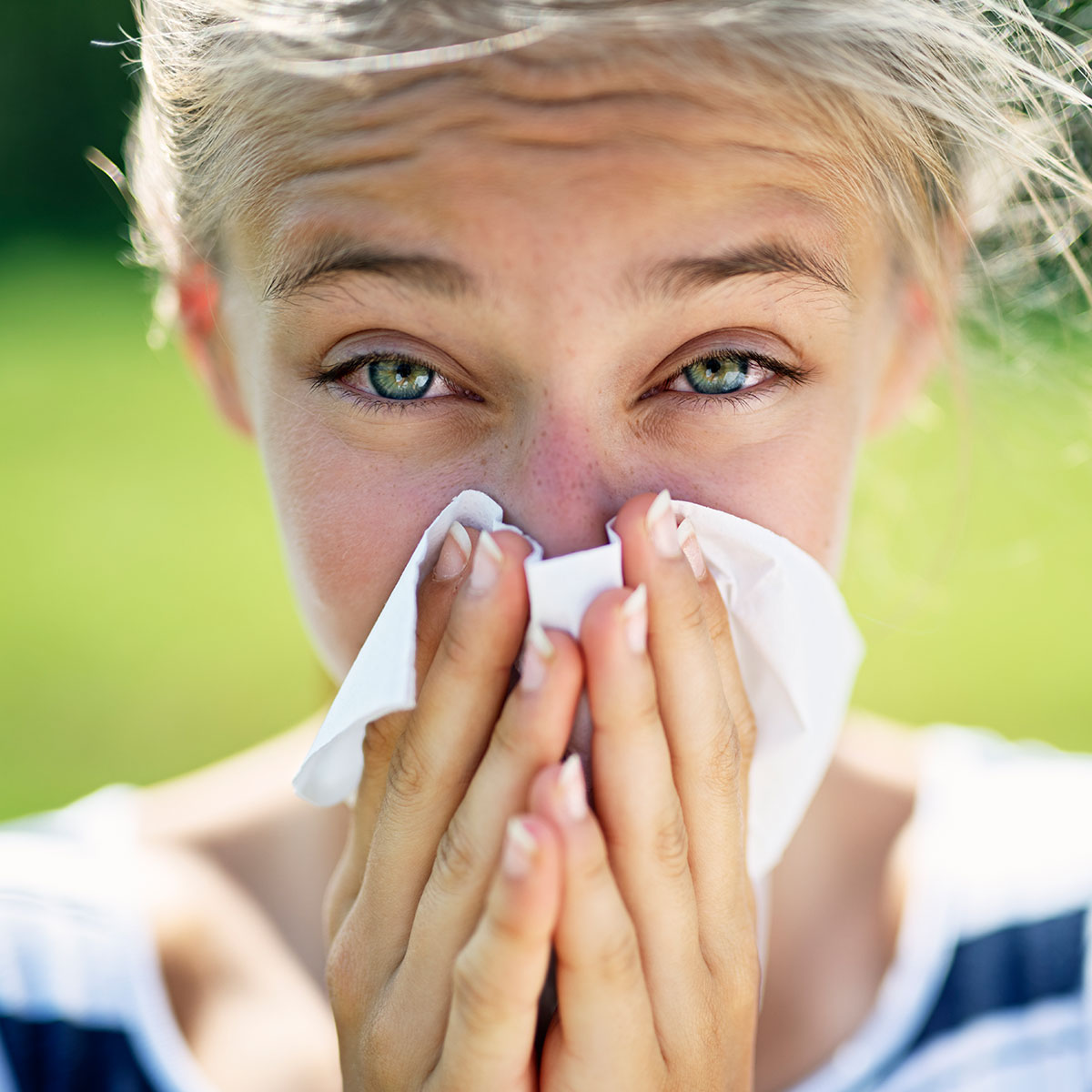 Frau mit roten Augen schnupft ins Taschentuch