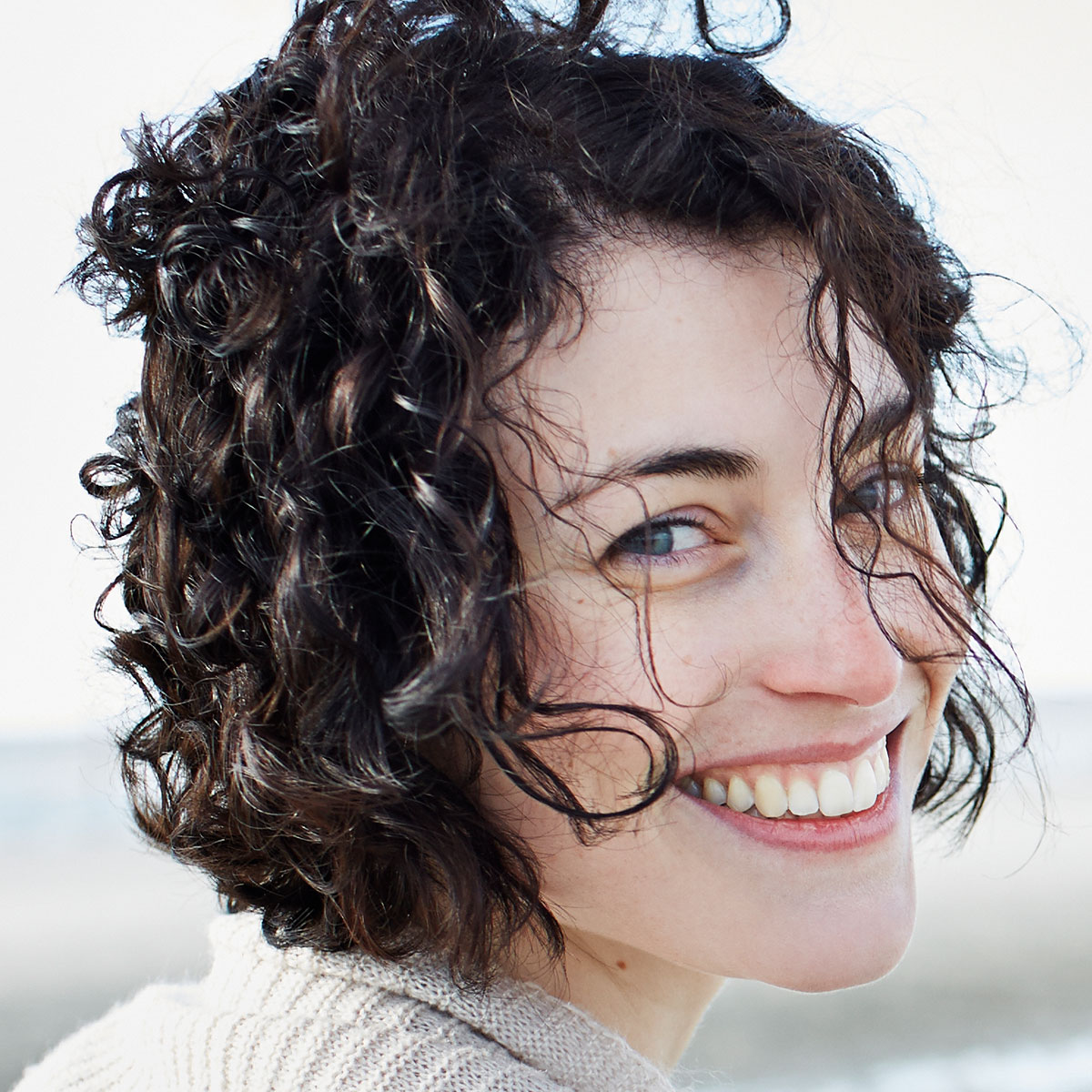 Frau mit braunen Locken lächelt in die Kamera