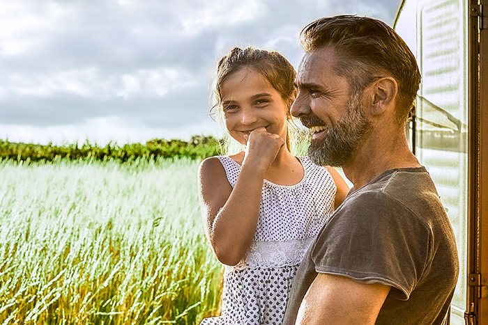 Mann tr&auml;gt Kind vor einer Wiese