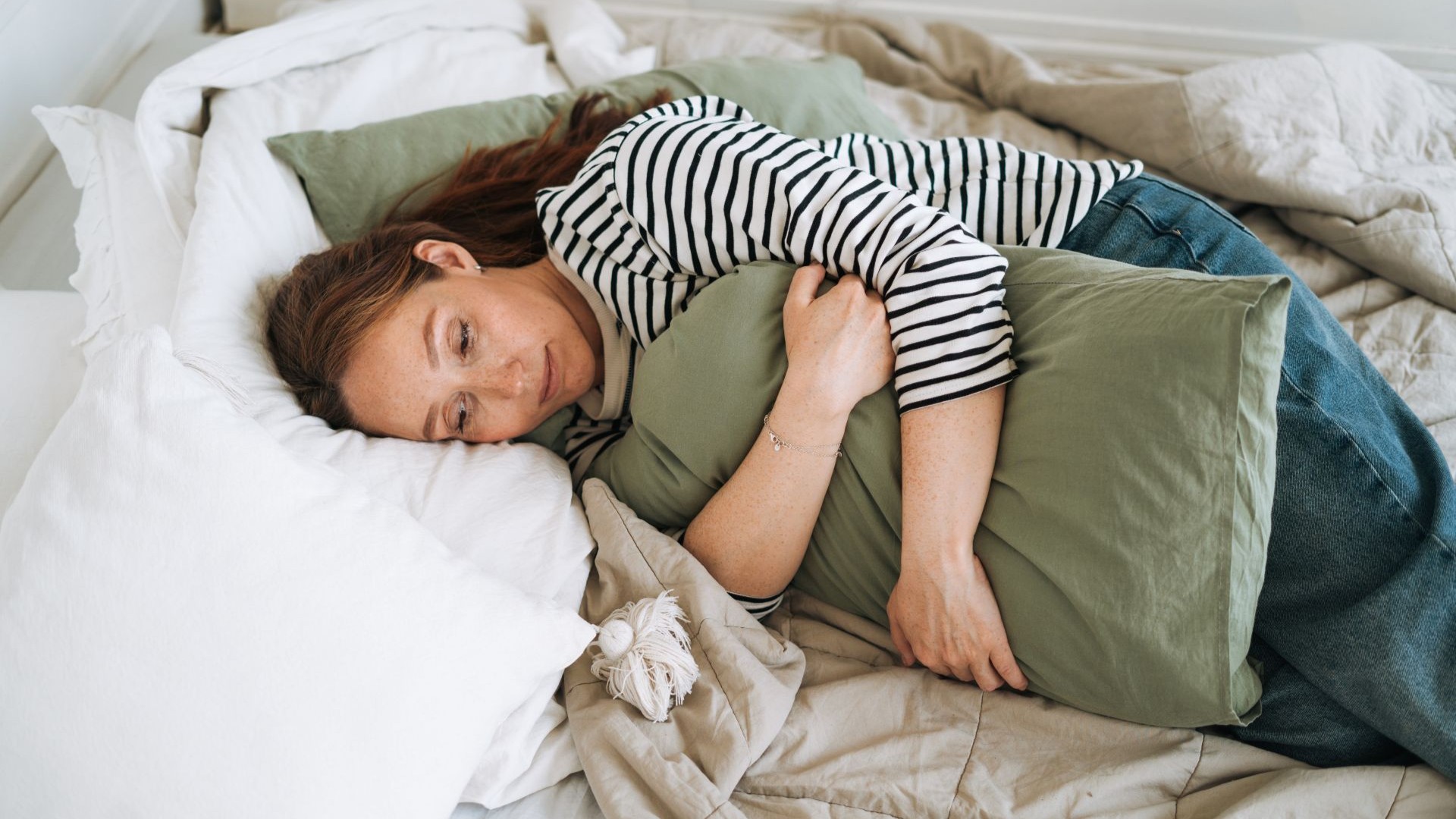 Rothaarige Frau liegt mit Unwohlsein im Bett