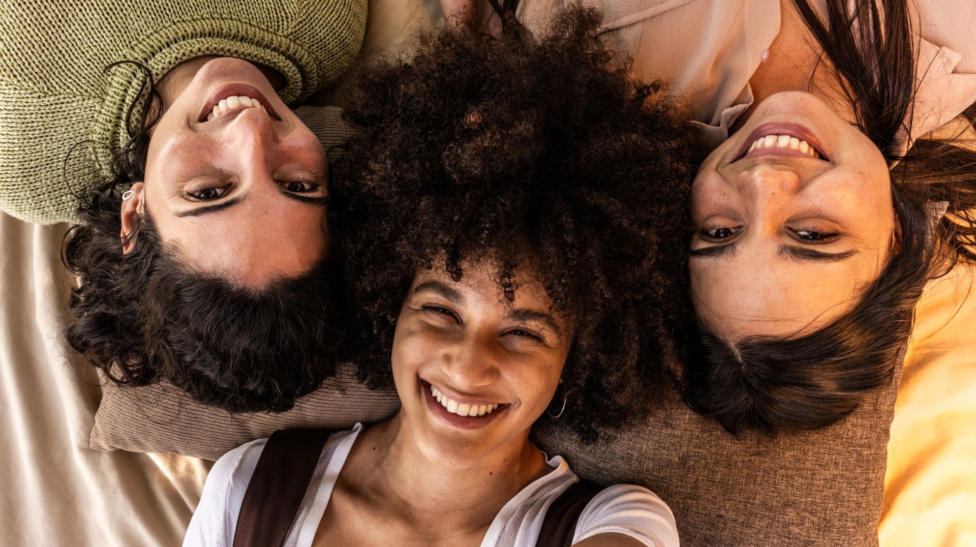 Drei Frauen liegen auf einer Decke und lachen in die Kamera