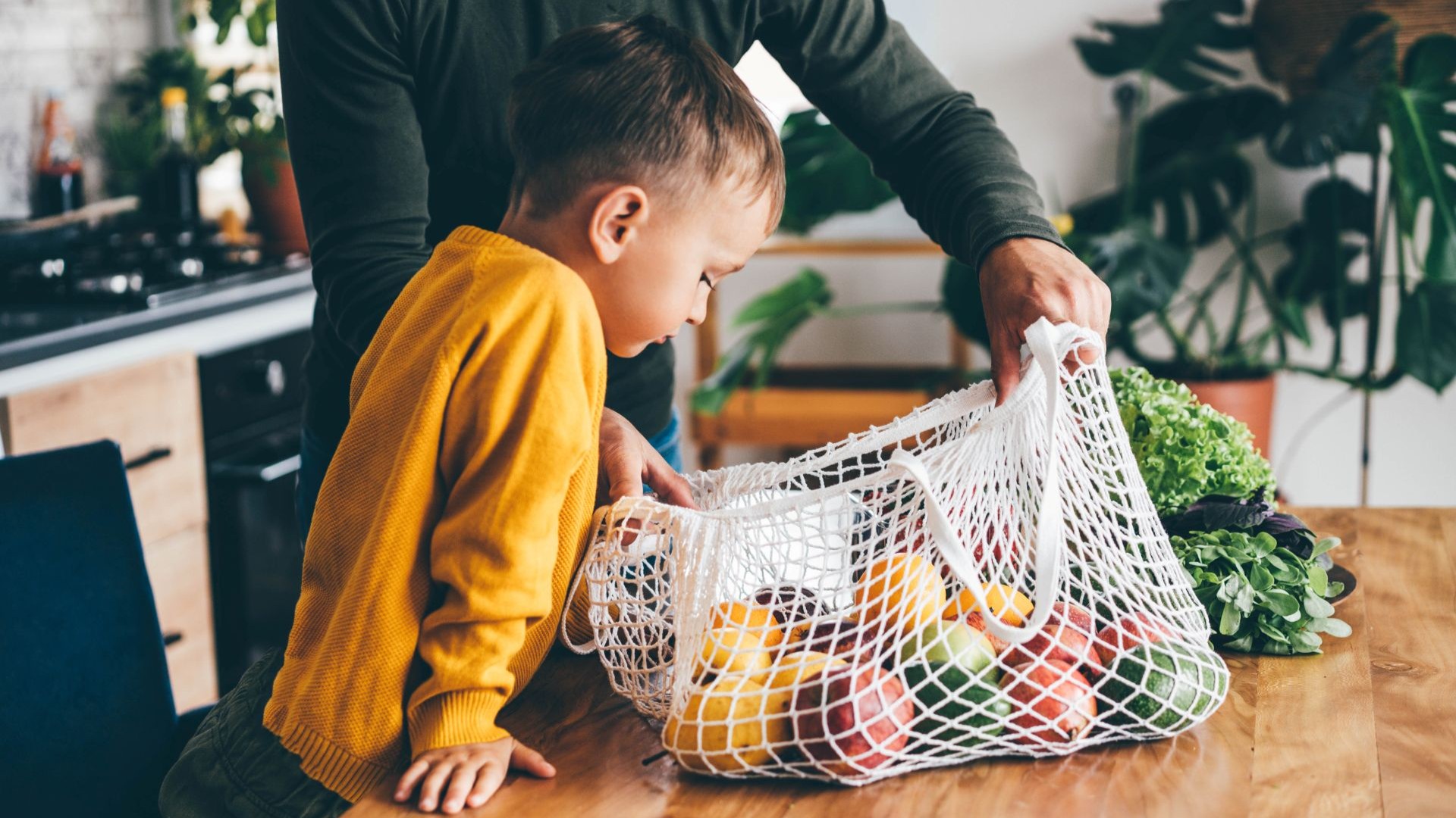 Kleiner Junge schaut in eine Tasche voller Obst und Gemüse