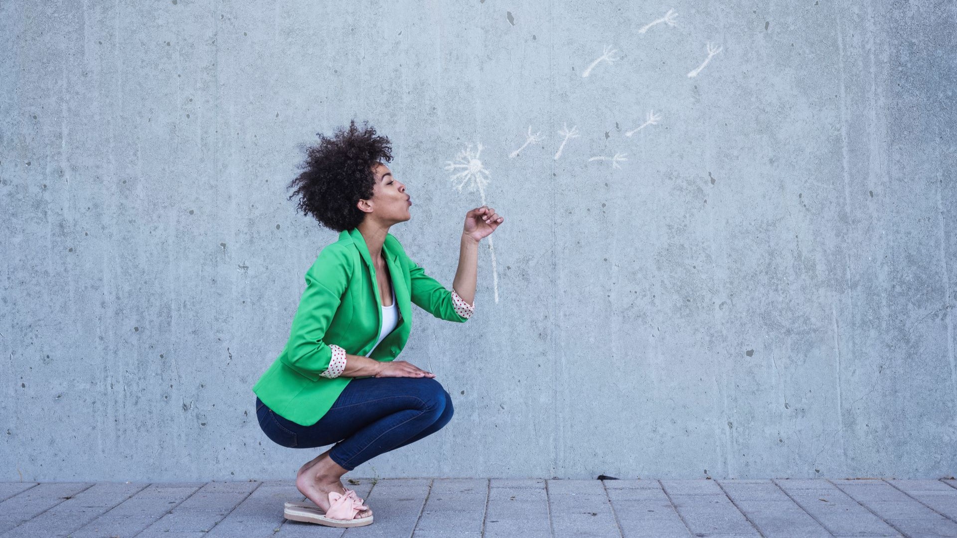 Frau hockt und pustet eine Pusteblume