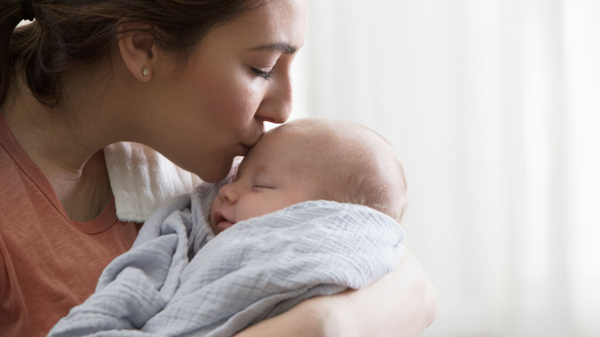 Braunhaarige Frau küsst Baby auf die Strin