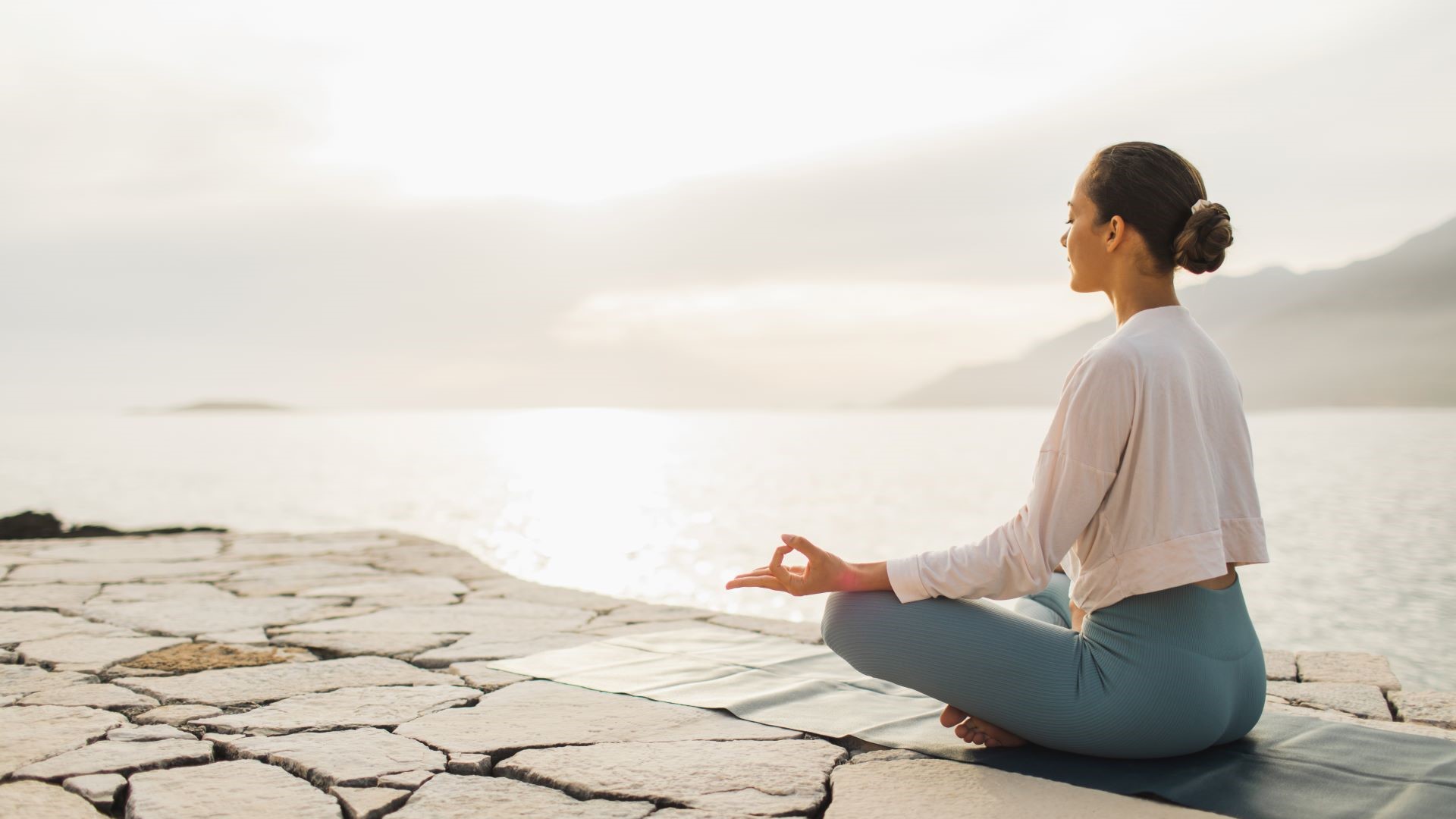 Braunhaarige Frau sitzt im Schneidersitz am Meer