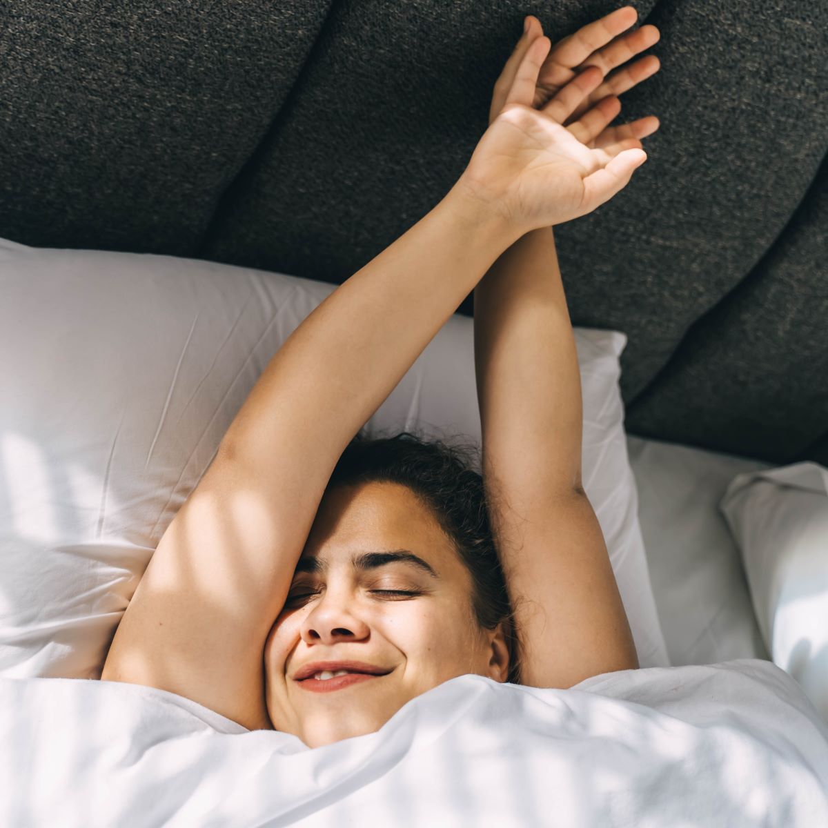 Frau liegt mit ausgestreckten Armen lächelnd im Bett Frau liegt mit ausgestreckten Armen lächelnd im Bett